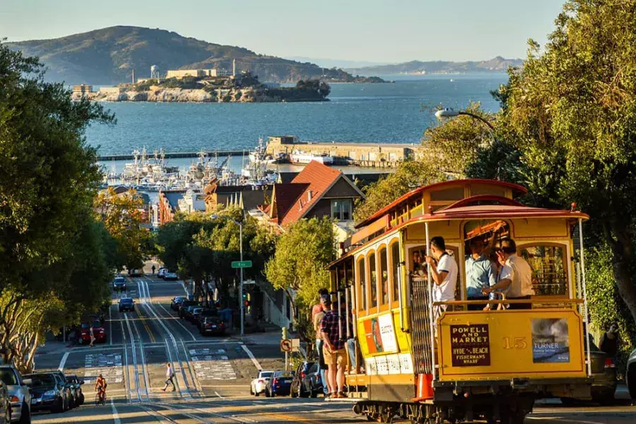 A Cable Car On A Street With A City And Water In The Background