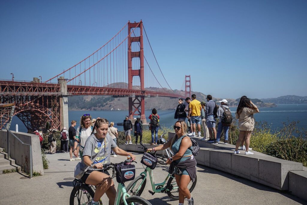 A Group Of People On Bicycles In Front Of A Bridge