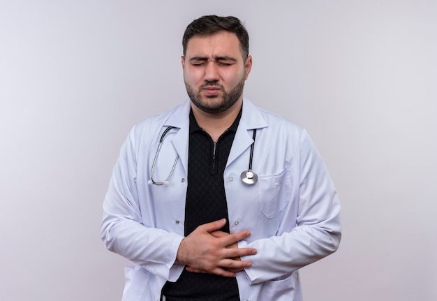 Young Bearded Male Doctor Wearing White Coat With Stethoscope Looking Unwell Touching His Belly Feeling Pain 141793 28238
